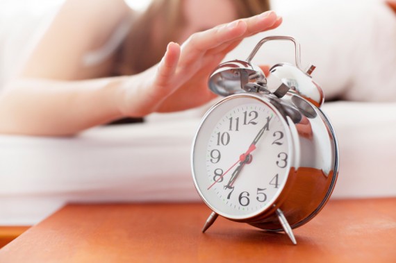 woman hitting snooze on alarm in the morning